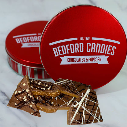 Red 'Bedford Candies' tin with chocolate pieces on a white background