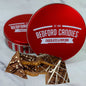 Red 'Bedford Candies' tin with chocolate pieces on a white background